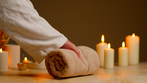 Person-Wearing-Robe-Picking-Up-Towel-At-Relaxing-Spa-Day-With-Lit-Candles-Dried-Grasses-And-Incense-Stick